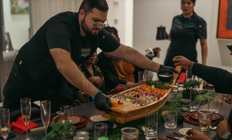 A chef presenting a sushi boat at a dinner table